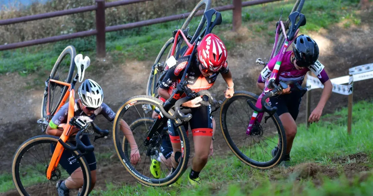 Trzy zawodniczki cyclocross niesa rowery na ramionach pod gore w trakcie wyscigu