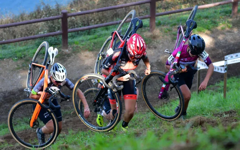 Trzy zawodniczki cyclocross niesa rowery na ramionach pod gore w trakcie wyscigu