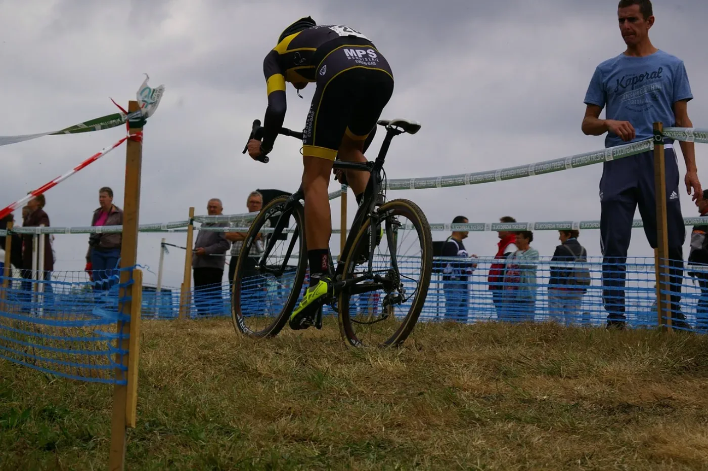 Zawodnik cyclocross w pełnym wysiłku na trawiastej trasie z trybunami i taśmami