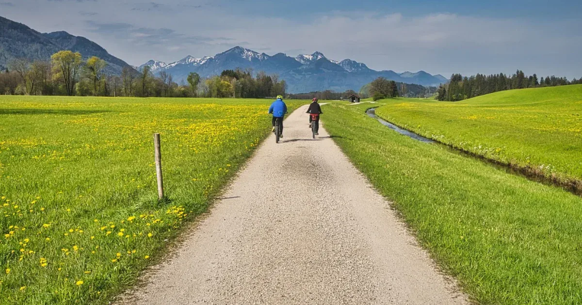Para rowerzystów gravelowych jadąca żwirową drogą wśród łąk z widokiem na góry