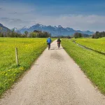 Para rowerzystów gravelowych jadąca żwirową drogą wśród łąk z widokiem na góry