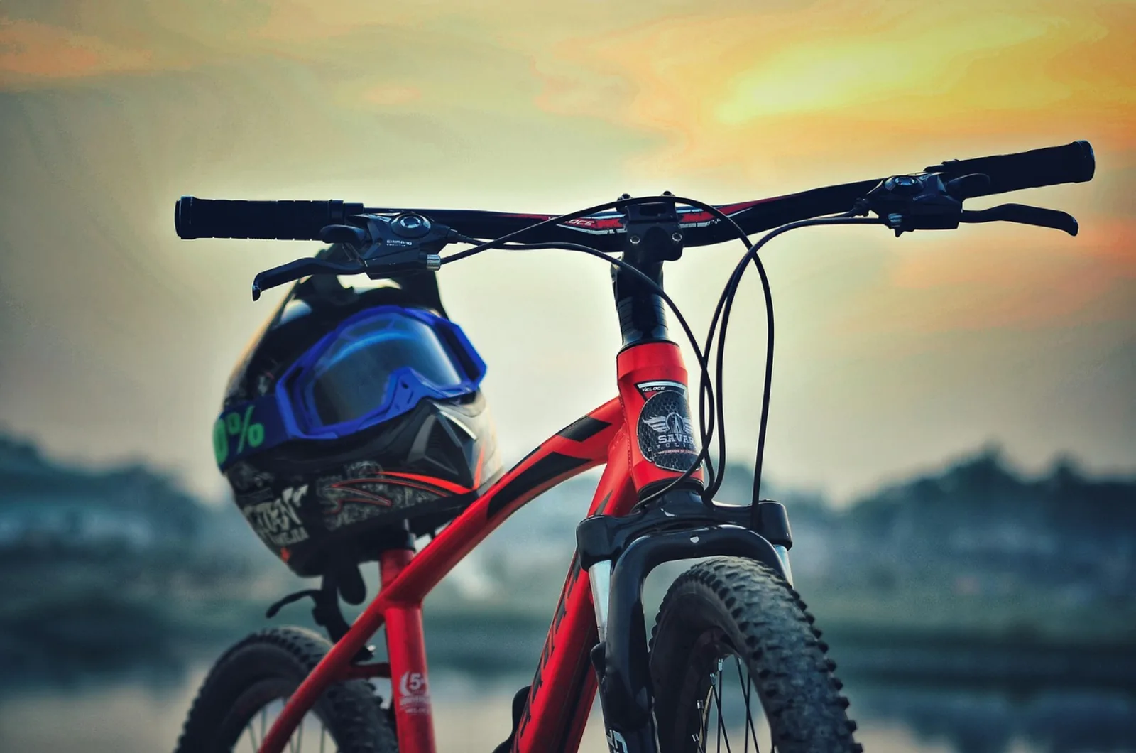 Czerwony hardtail MTB z czarnym widelcem amortyzowanym i kaskiem pełnotwarzowym wiszącym na ramie