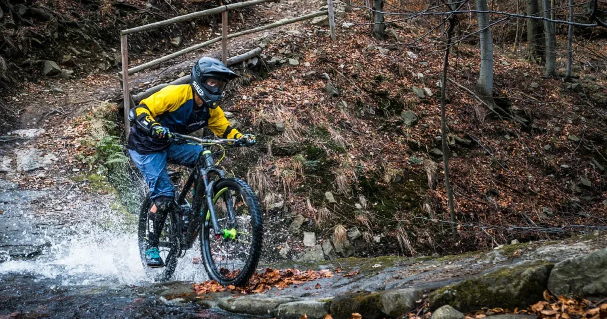 Rowerzysta MTB enduro w pełnym sprzęcie pokonujący strumień w lesie