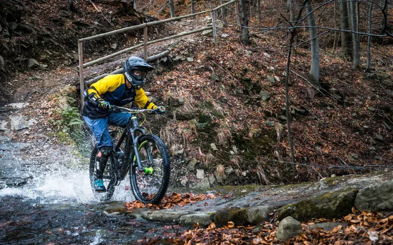 Rowerzysta MTB enduro w pełnym sprzęcie pokonujący strumień w lesie