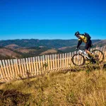Rowerzysta MTB jedzie singletrackiem na zboczu góry przy drewnianym ogrodzeniu