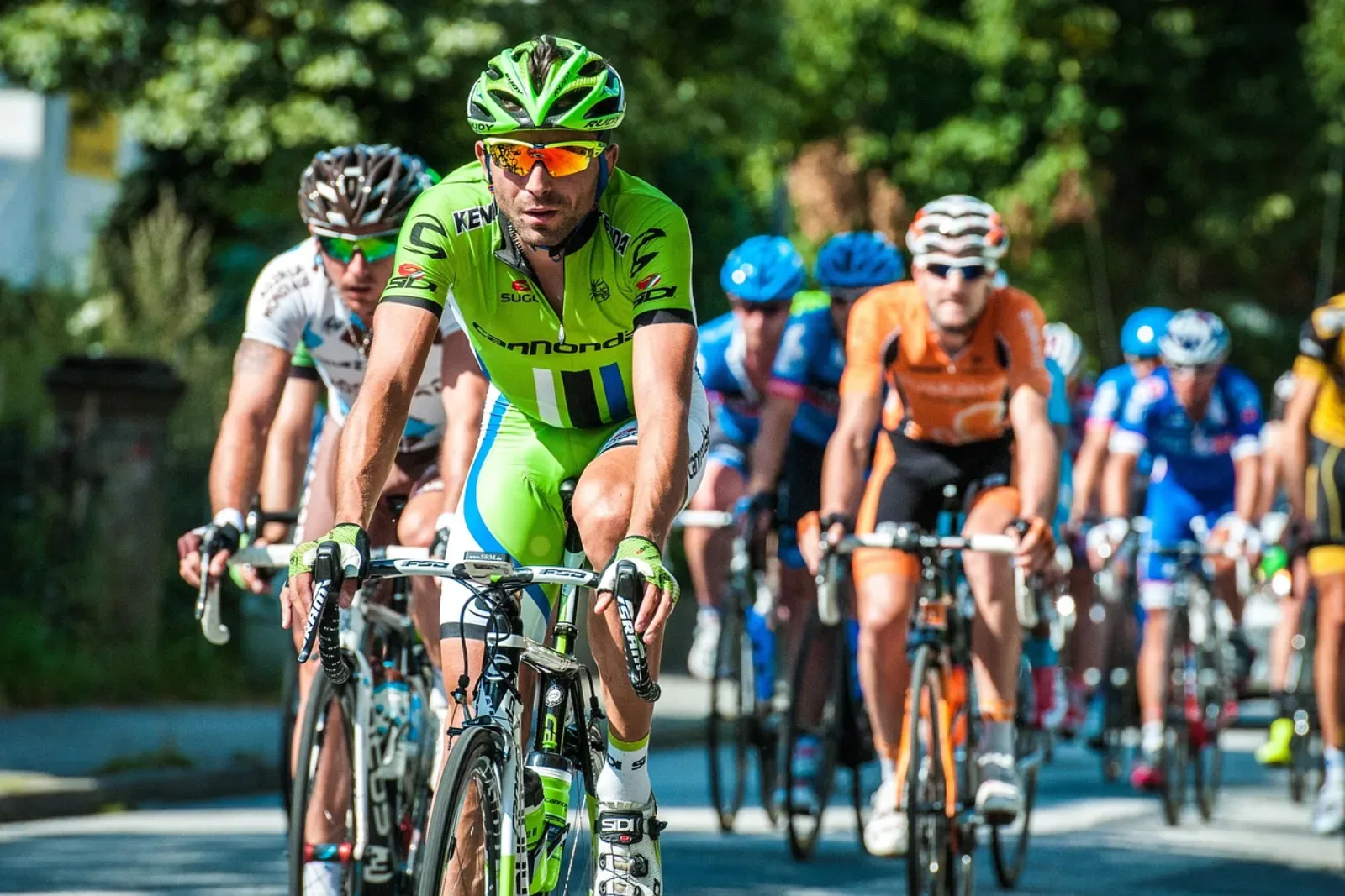 Peloton kolarski na szosie z rowerzystami w kolorowych koszulkach drużynowych