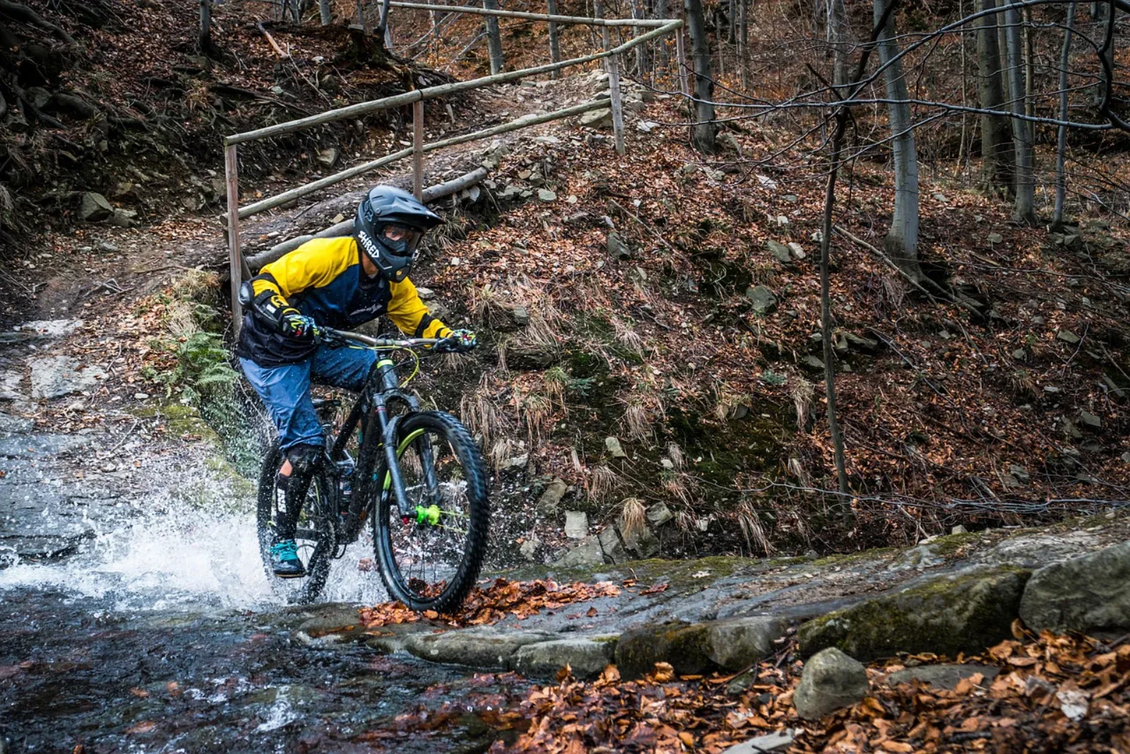 Rowerzysta enduro w żółtej kurtce na MTB pełnozawiasowym przejeżdża przez strumień w Beskidach