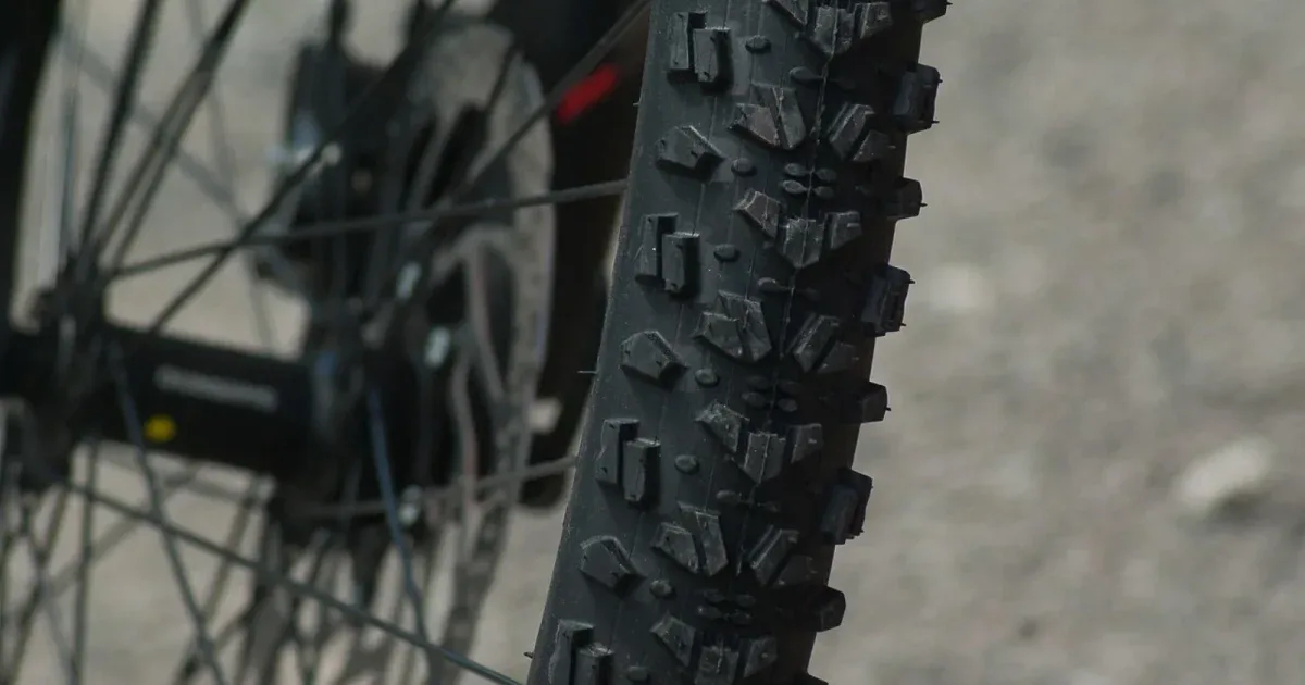 Zbliżenie na bieżnik opony MTB z agresywnymi kostkami i tarczę hamulcową w tle