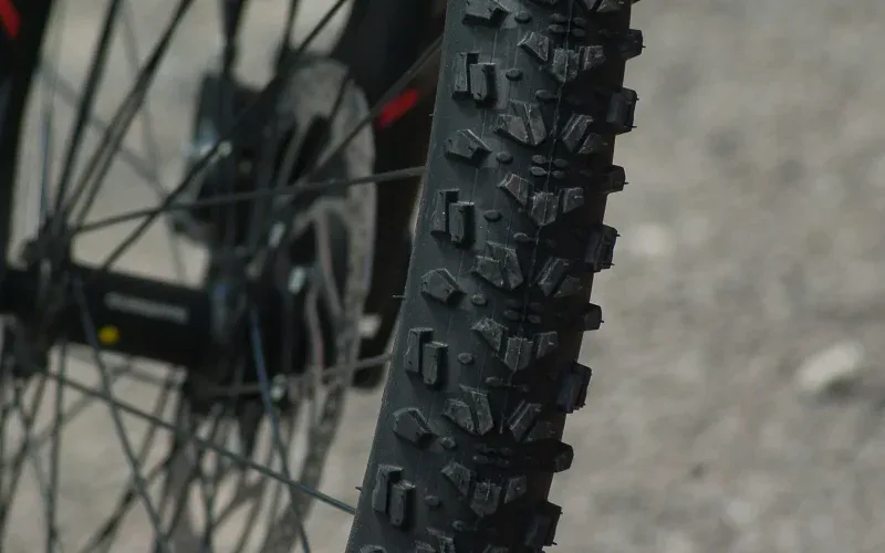 Zbliżenie na bieżnik opony MTB z agresywnymi kostkami i tarczę hamulcową w tle