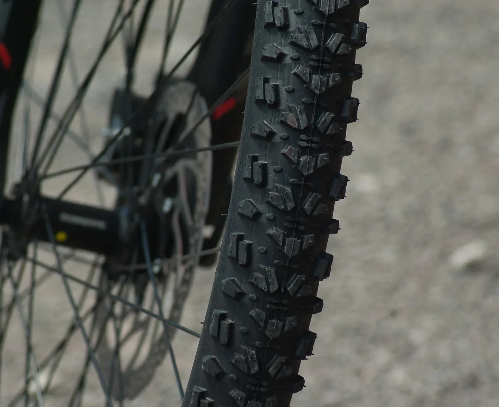 Zbliżenie na bieżnik opony MTB z agresywnymi kostkami i tarczę hamulcową w tle