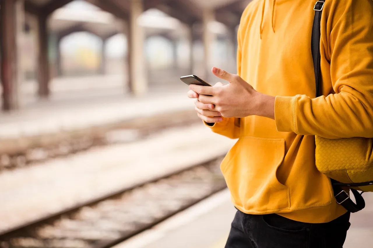 Pasażer sprawdza rozkład jazdy w telefonie, stojąc na peronie