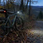 Rower gravel z włączoną lampką przednią i czerwoną lampką tylną na leśnej drodze o zmierzchu