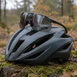 Okulary rowerowe z ciemnym szkłem położone na kasku rowerowym na pniu w jesiennym lesie